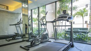Un gimnasio con cintas de correr, un espejo grande y amplias ventanas que dan a una vista de palmeras.