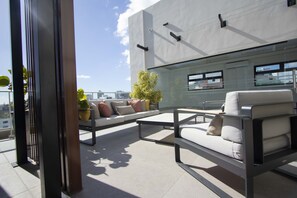 Een moderne buitenruimte met een bank, lounge stoelen en een glazen afscheiding.