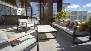 Un área de estar al aire libre y moderna con un sofá, sillas y una mesa, rodeada de plantas y un separador de madera.