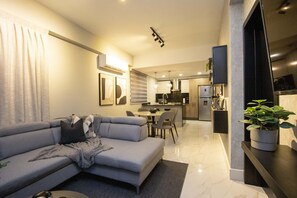 Een moderne woonkamer met een grijze bank, een eethoek en een keuken op de achtergrond.