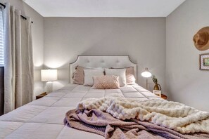 A bedroom with a large bed, a headboard, two bedside tables with lamps, and a wall-mounted hat. - Pool Playhouse: FirePit, Grill, Billiards & Jenga (Richardson)