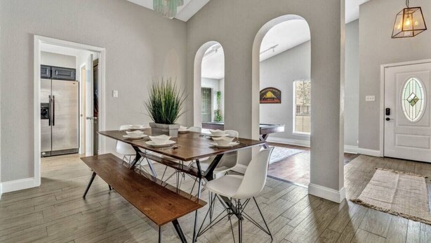 A spacious dining area with a wooden table and chairs, a bench, and a potted plant. - Pool Playhouse: FirePit, Grill, Billiards & Jenga (Richardson)