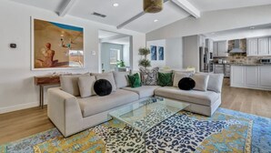 Un salon spacieux avec une table basse en verre, un canapé d’angle beige et un tapis aux motifs colorés.