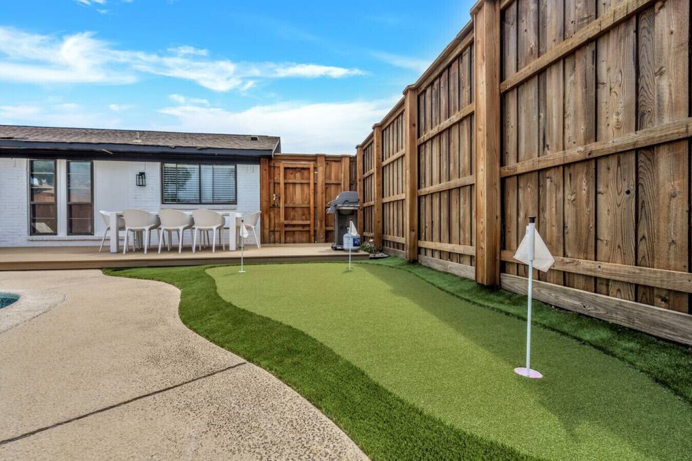A backyard with artificial grass, a patio with chairs, and a wooden fence.