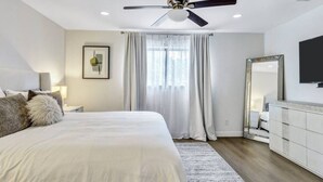 Une chambre moderne avec un grand lit, un ventilateur de plafond, une télévision et un miroir.