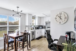 A modern kitchen with white cabinets, a large wall clock, and a dining area with a wooden table and chairs.