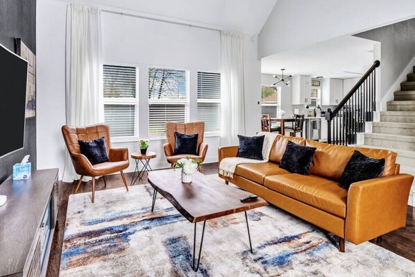 A modern living room with a brown leather sofa, two leather armchairs, a wooden coffee table, and a patterned rug.