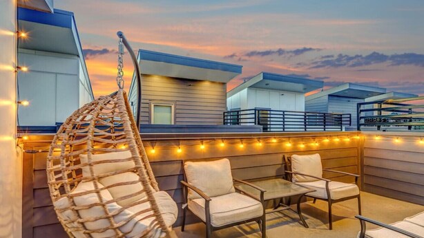 Eine Dachterrasse mit Hängesessel, zwei gepolsterten Stühlen und einer Lichterkette.