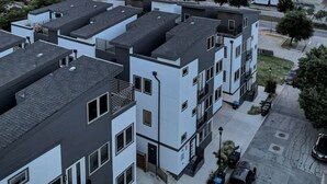 Ein moderner Wohnkomplex mit mehreren Wohneinheiten, einem Parkplatz und Blick auf die Straße.