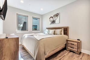 Une chambre avec un grand lit, des tables de chevet en bois, une télévision et deux fenêtres.