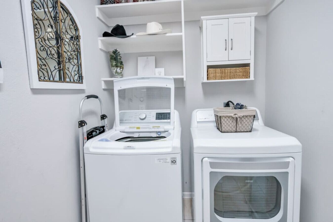 A laundry area with a front-loading washer and dryer, a shelf with hats, and a decorative window.