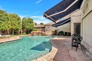 Una piscina con cascada, rodeada de un patio con mobiliario exterior.
