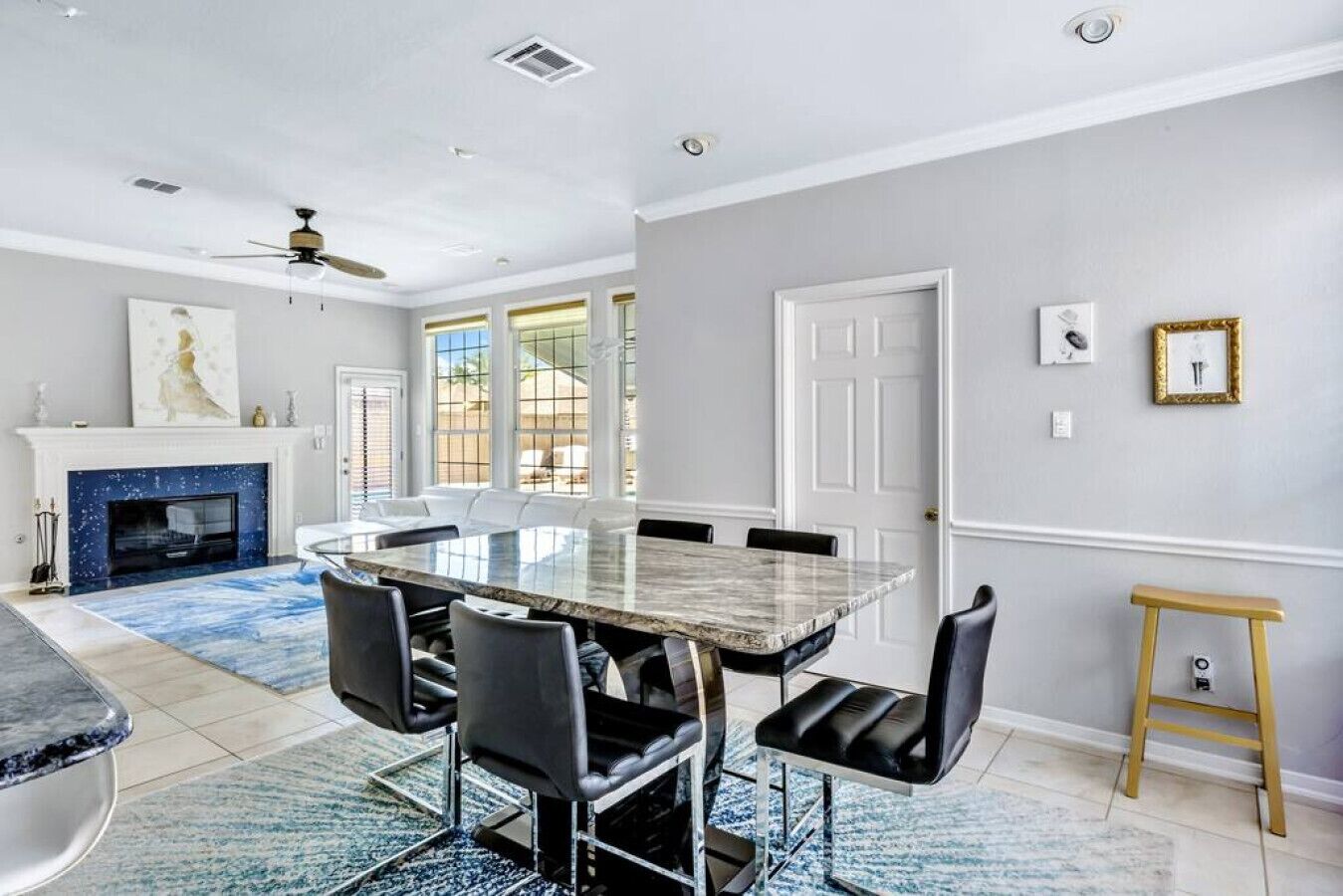 A spacious dining area with a marble table, black chairs, and a blue patterned rug.