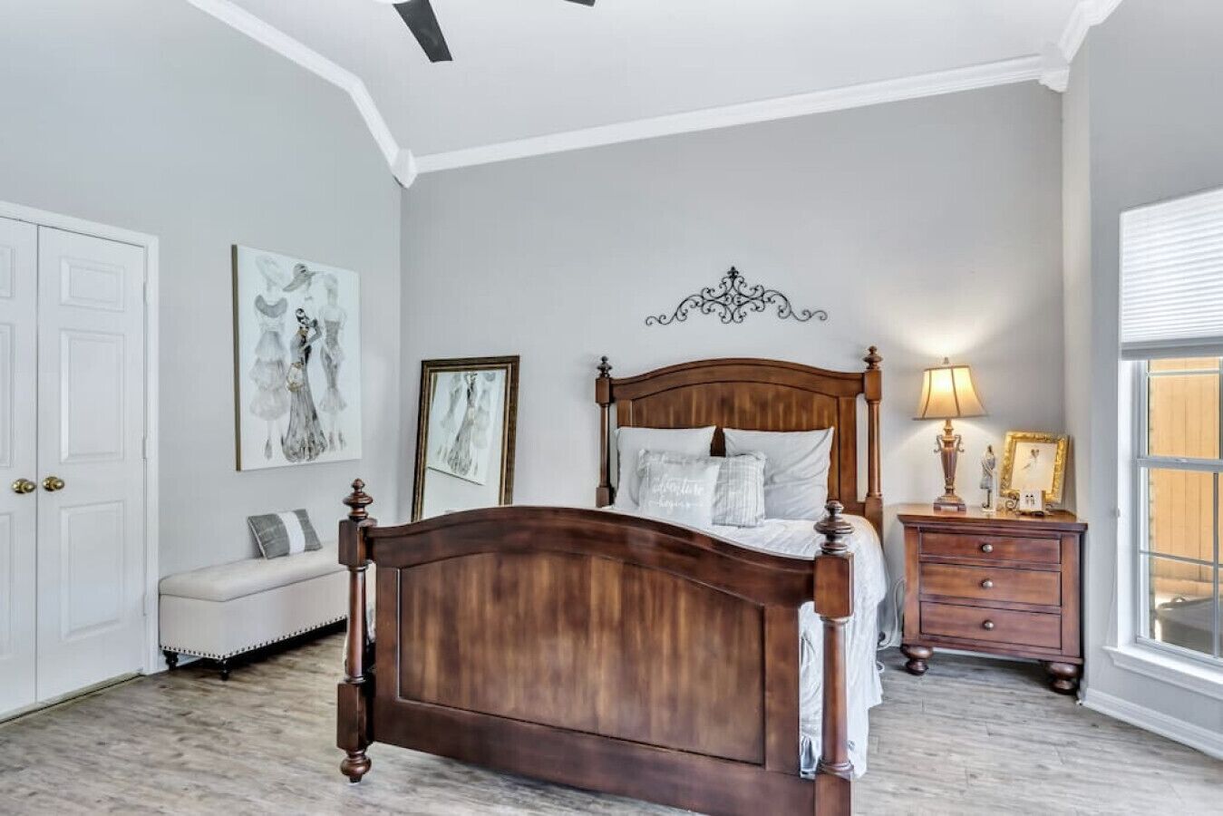A bedroom with a wooden bed, a nightstand, a bench, and artwork on the walls.