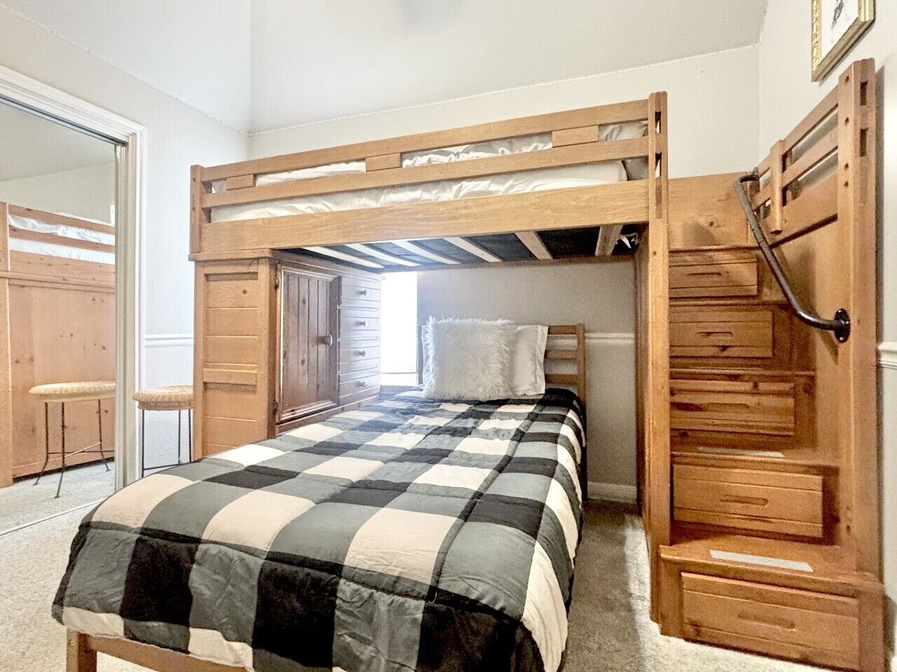 A bunk bed with a checkered bedspread, a wooden ladder, and a small desk with drawers.