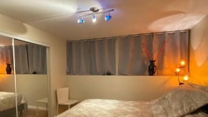 A bedroom with a bed, a chair, a mirror, and a window with curtains. - Cozy Sunset suite (San Francisco)