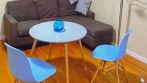 A living room with a brown sofa, two blue chairs, a small round table with a blue object, and a tall floor lamp with colorful decorations. - Cozy Sunset suite (San Francisco)