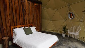 Ein Bett mit weißer Bettwäsche, einem Holzkopfteil und einem kleinen Nachttisch mit einer Pflanze.