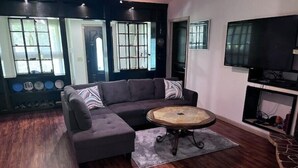 Una sala de estar con un sofá modular, una mesa de centro redonda y un televisor de pantalla plana montado en la pared.