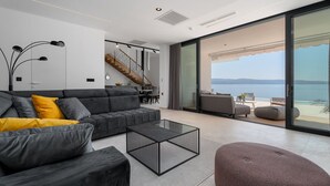 Una sala de estar moderna con un sofá gris, una mesa de centro y vista al mar a través de amplios ventanales.