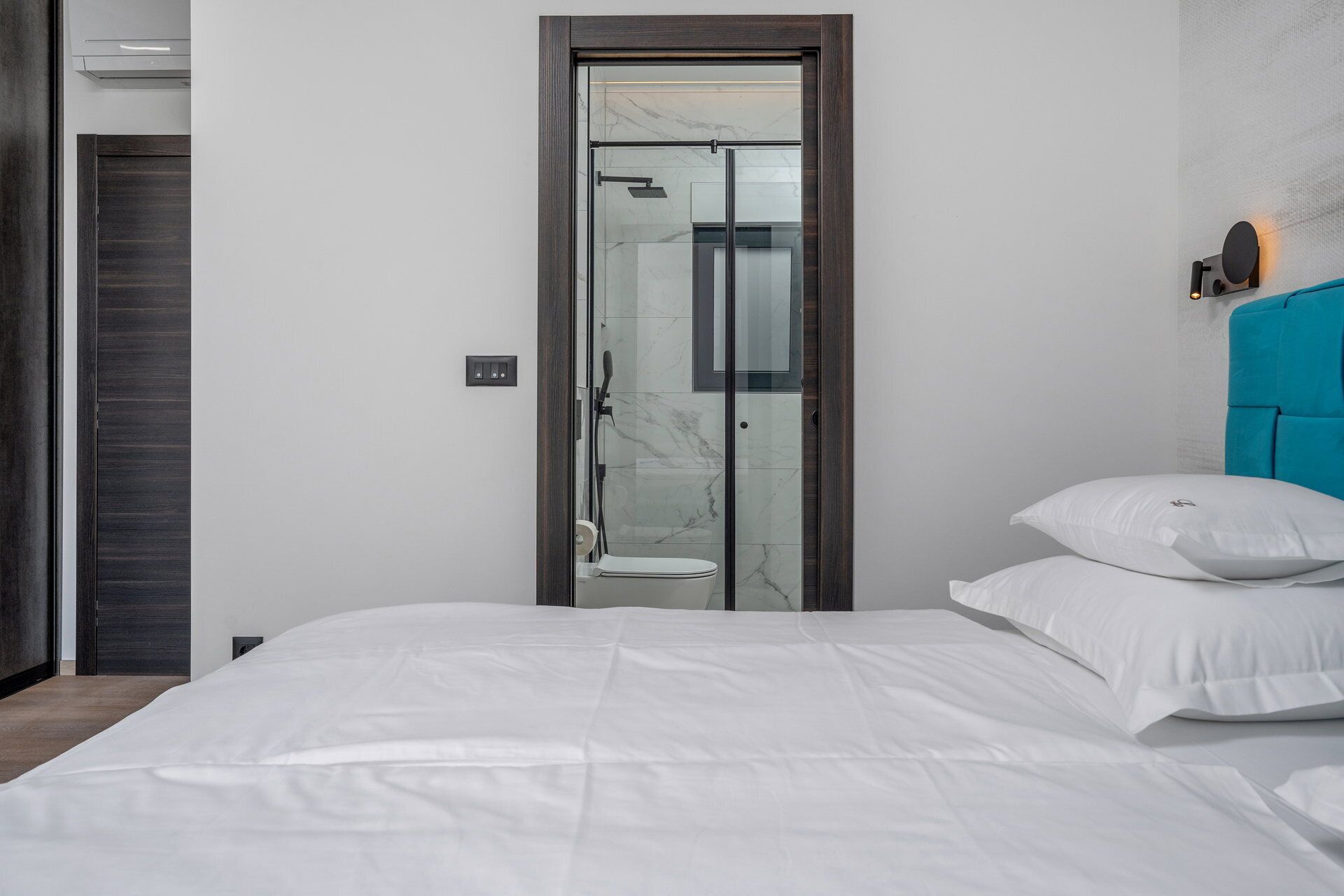 Une chambre moderne avec un grand lit, une porte de douche en verre et une tête de lit de couleur turquoise.