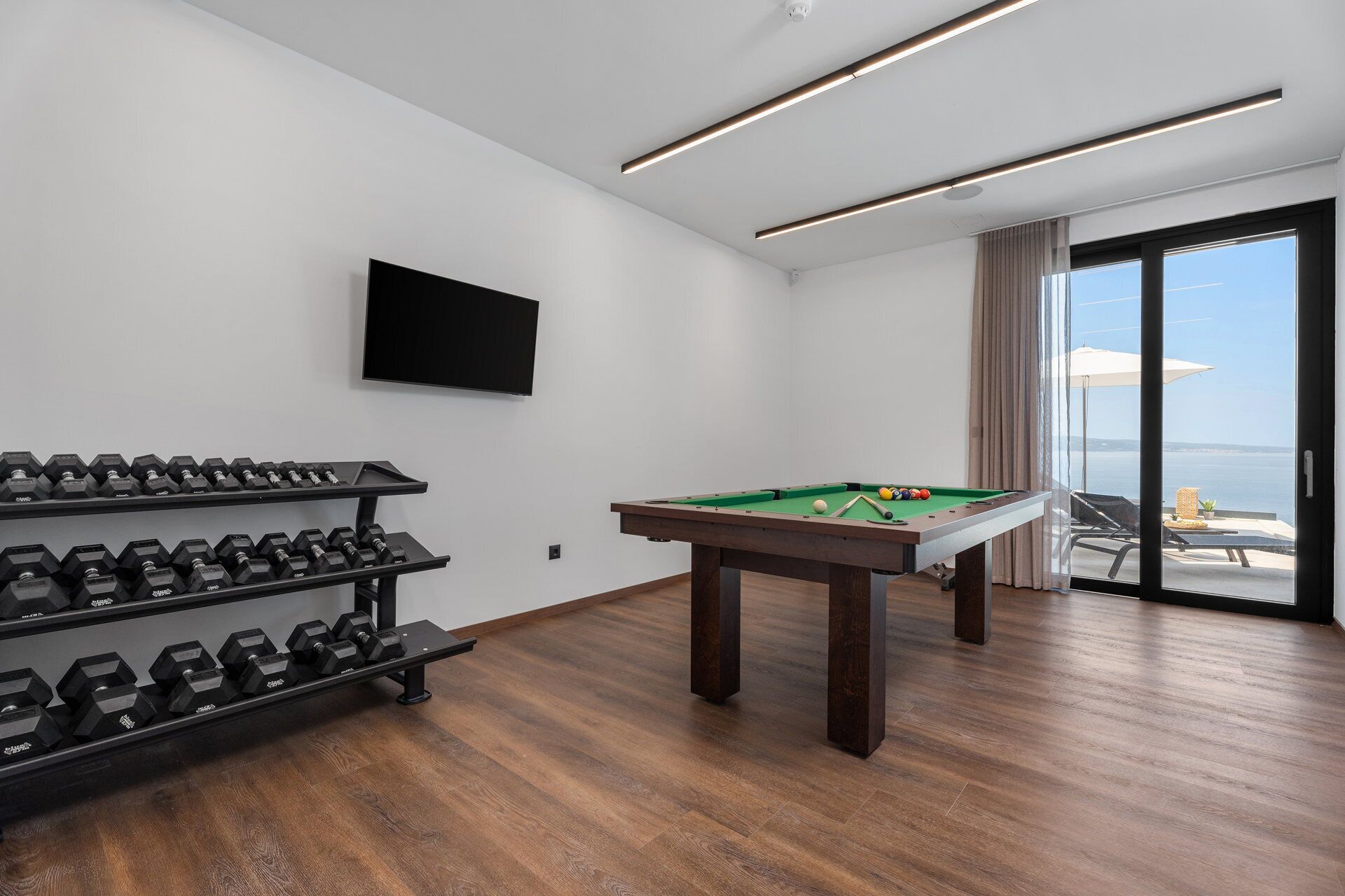 Une pièce équipée d’une table de billard, d’un téléviseur fixé au mur et d’un porte-haltères.