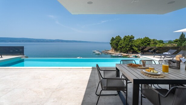 A poolside area with a view of the sea, outdoor seating, and a breakfast setup. - Beachfront Villa Cordelia with Pool (Omiš)