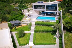 Une maison moderne à deux étages, dotée d’une piscine, d’un patio couvert et d’un jardin bien entretenu.