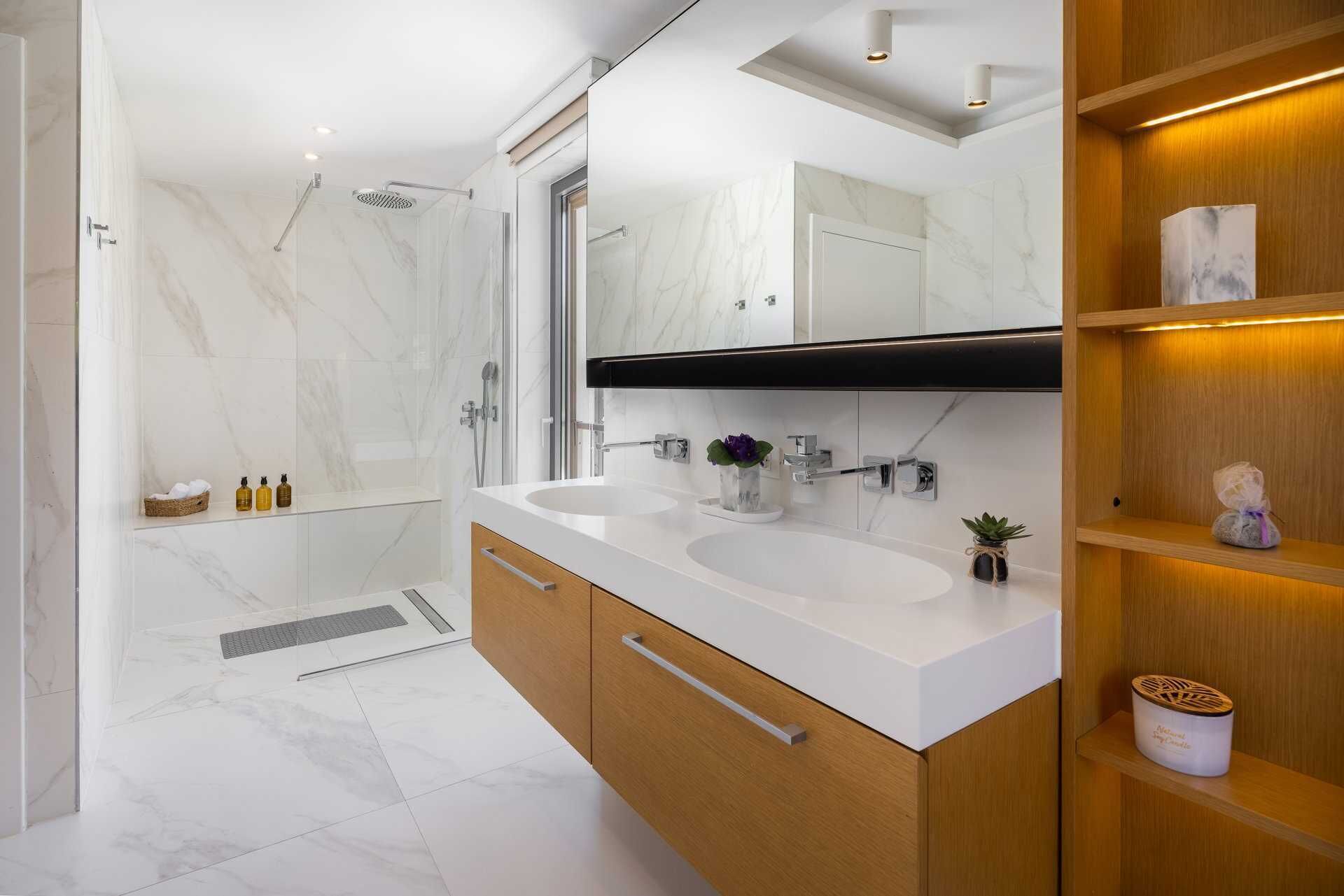 Een moderne badkamer met twee wasbakken, een douche en een houten wastafelmeubel.
