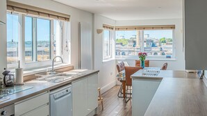 Een moderne keuken met grote ramen, een vaatwasser en een eethoek met een tafel en stoelen.