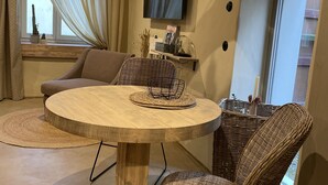 A cozy living room with a round wooden table, wicker chairs, a mounted TV, and a window with curtains. - Unterkunft Nähe Magdeburg und Oschersleben Motorpark (Wanzleben-Börde)