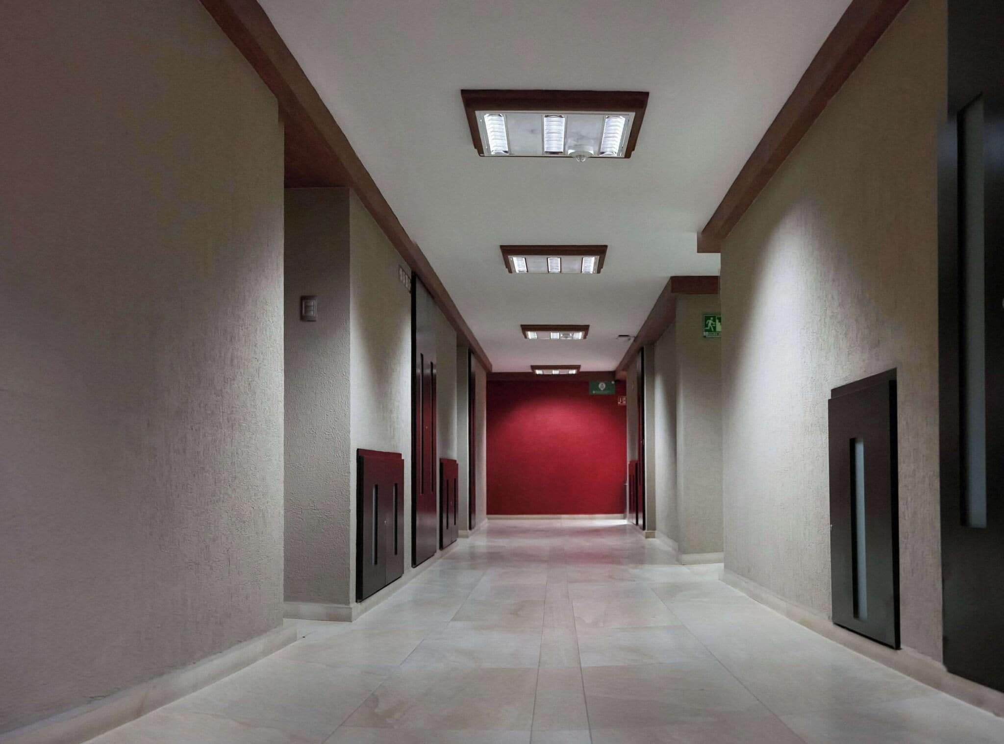A corridor with a red carpet, recessed lighting, and a door on the right.