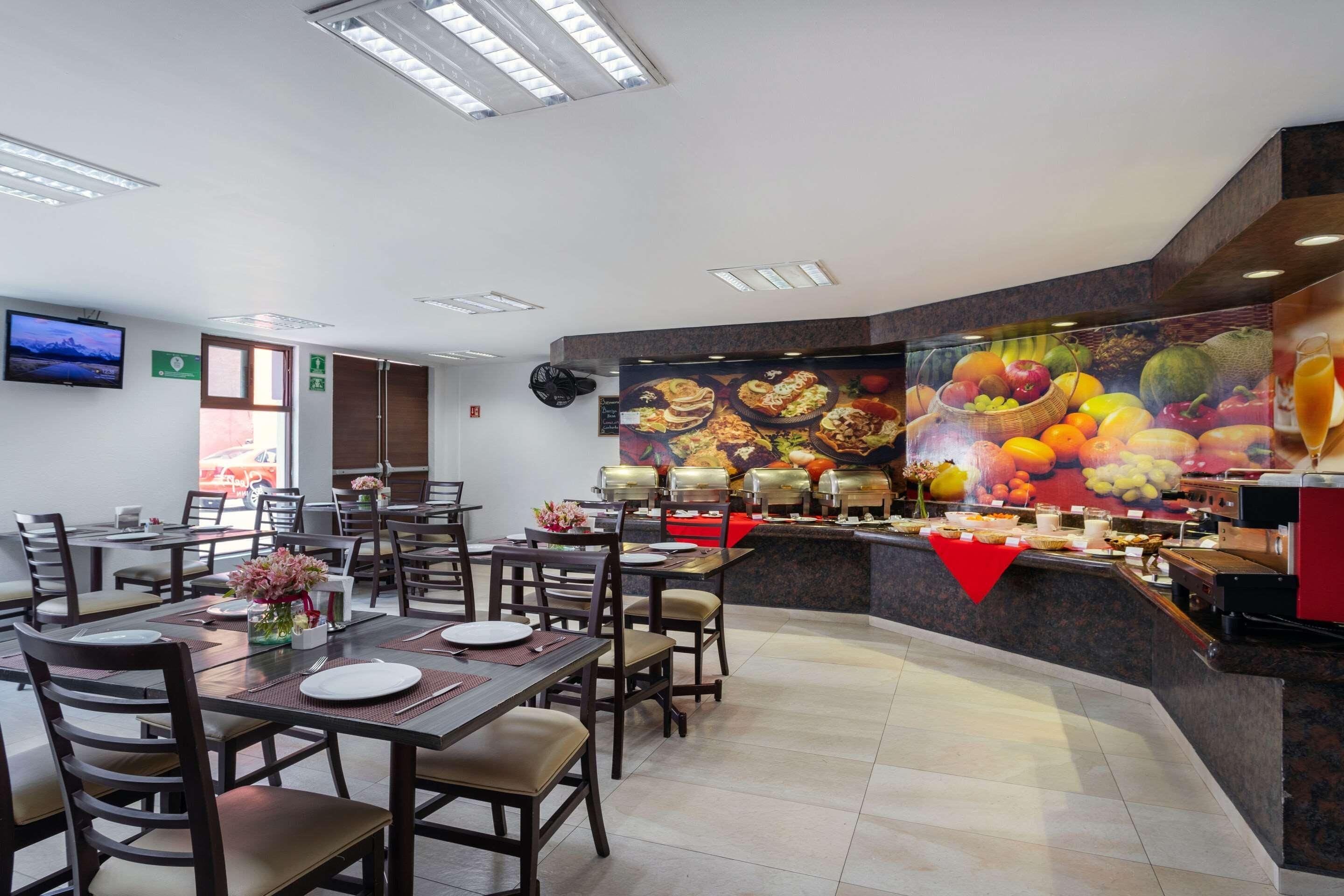 A restaurant with multiple dining tables, chairs, a buffet counter, and a television screen on the wall.