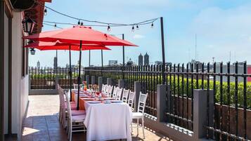 An outdoor dining area with tables and chairs, a red umbrella, and a city view.