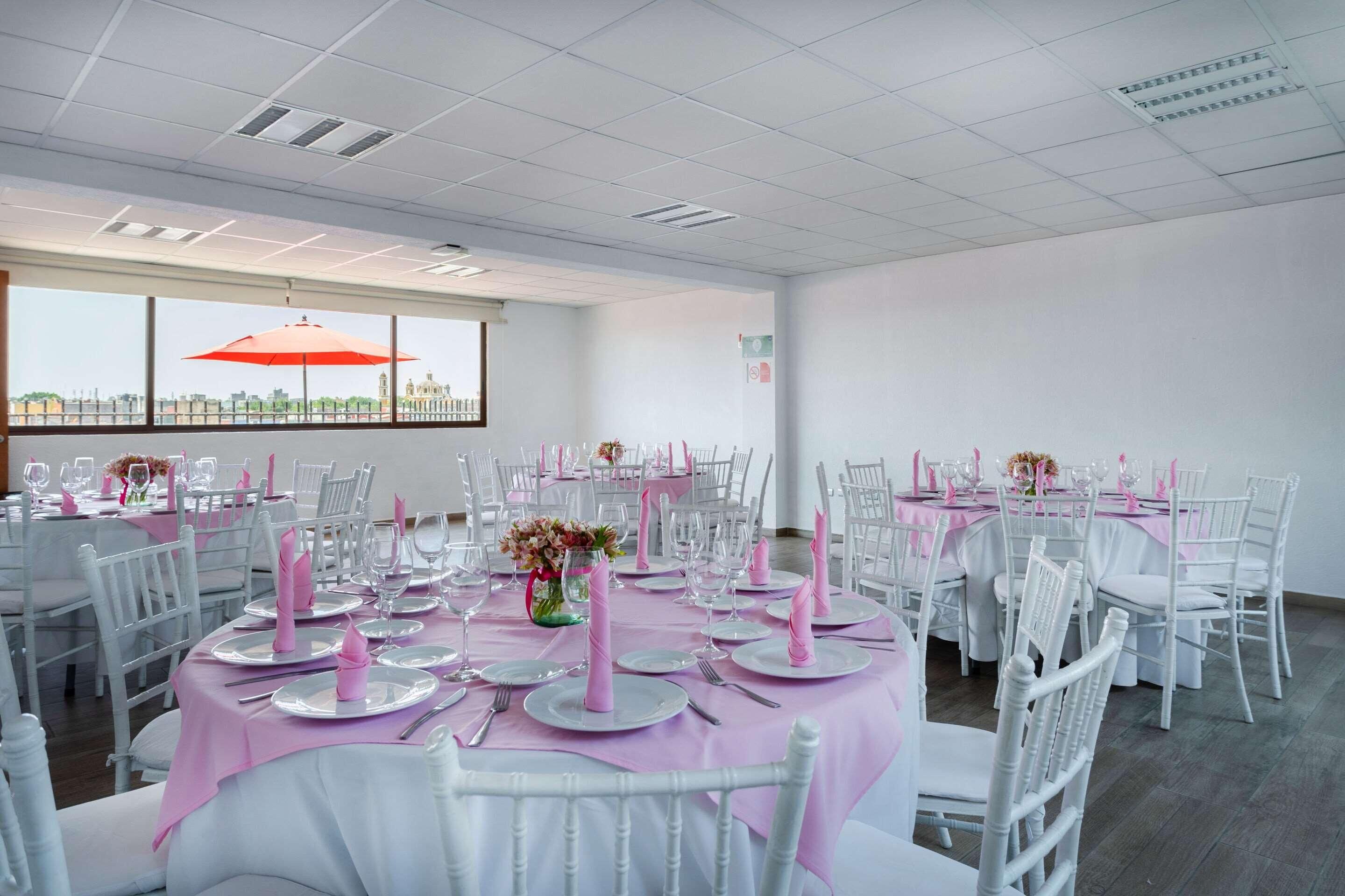 Een feestzaal met ronde eettafels, witte stoelen en een groot raam met een parasol.