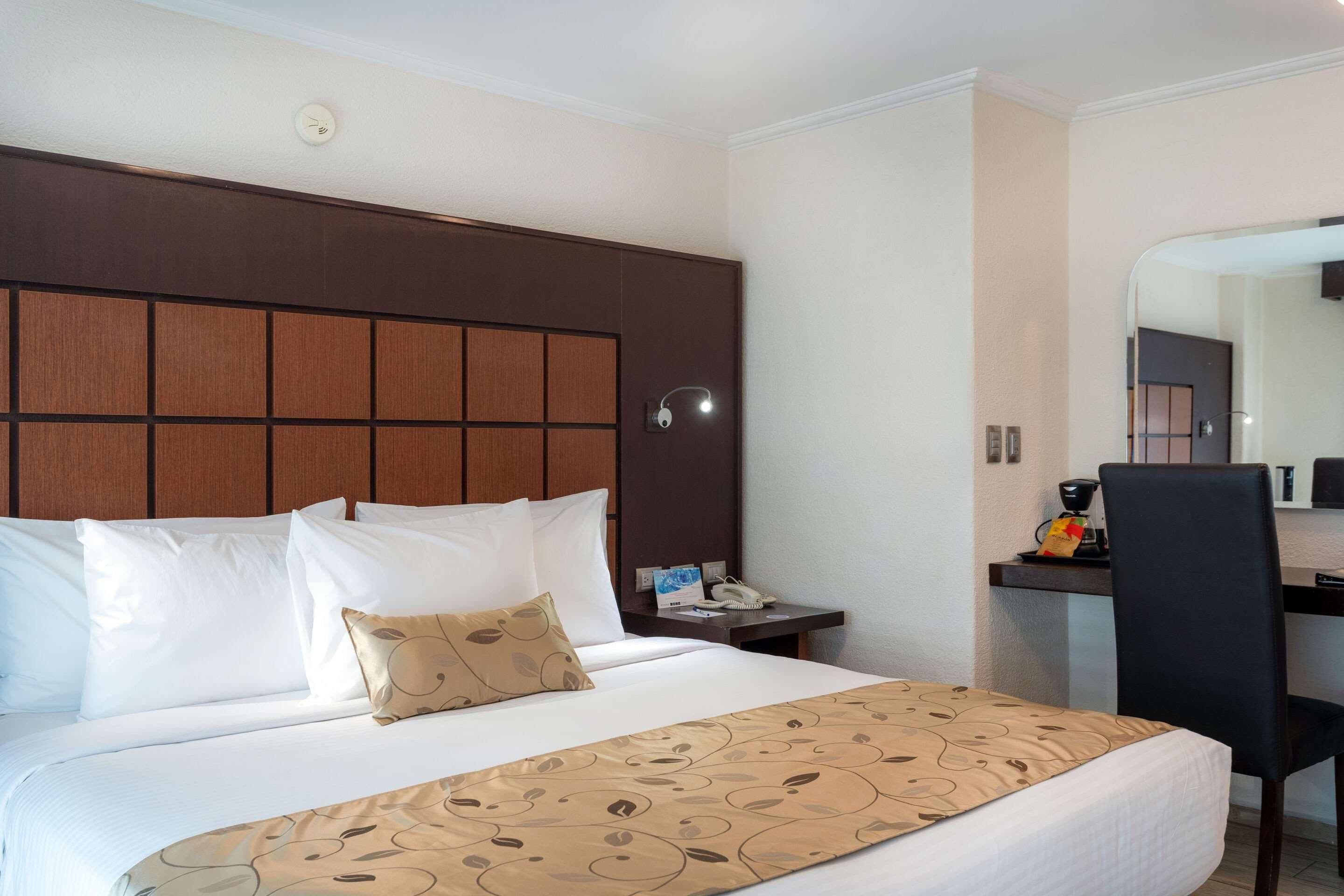 A hotel room with a bed, a desk, a chair, a telephone, and a mirror.
