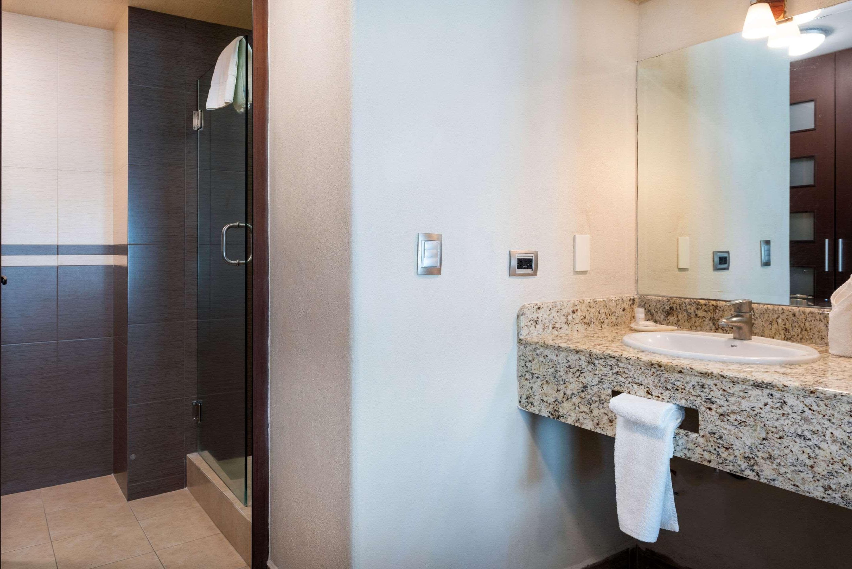 A modern bathroom with a glass shower enclosure, a granite countertop sink, and a large mirror.