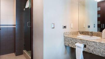 Un baño moderno con cabina de ducha de vidrio, lavamanos de encimera de granito y un espejo grande.