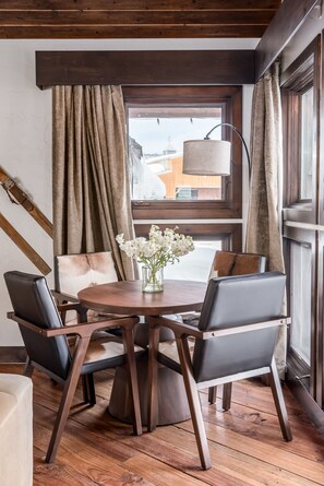 Een eetruimte met een ronde houten tafel, vier stoelen, een vaas met bloemen en uitzicht buiten door een raam met gordijnen.