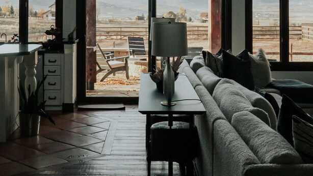 Ein Zimmer mit großem Fenster, einer Couch, einem Tisch und einer Lampe.