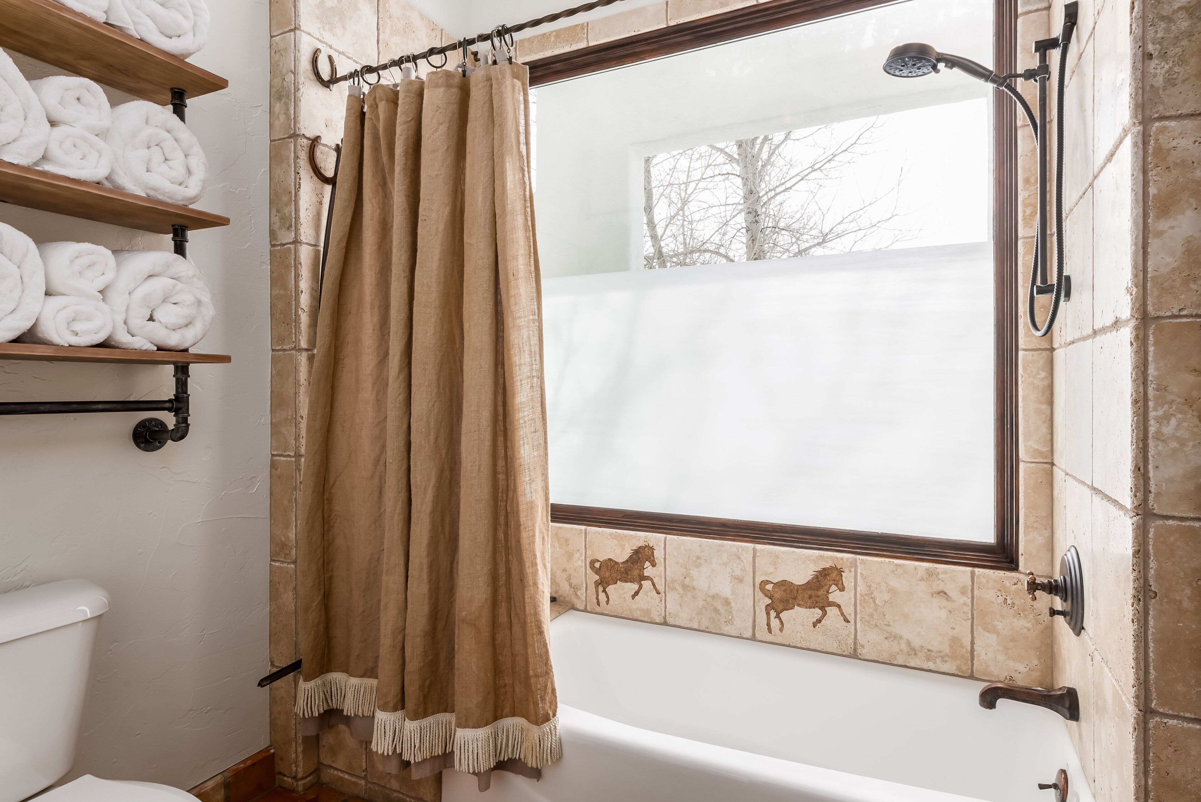A bathroom with a bathtub, a shower, and a toilet. There are towels on a shelf and a curtain.