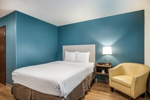 A hotel room with a bed, a chair, a nightstand, and a lamp.