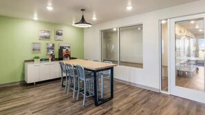 A conference room with a wooden table, chairs, a white cabinet, framed pictures, and a large window. - Woodspring Suites Downers Grove - Chicago (Downers Grove)