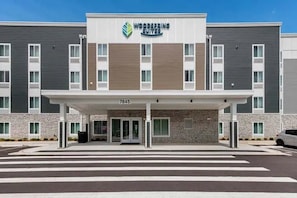 Un hotel moderno con entrada cubierta, fachada de piedra y un letrero que dice 'Woodspring Suites'.