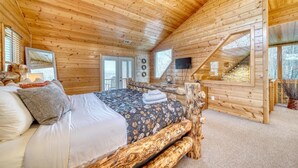 A wooden cabin bedroom with a bed, a TV, and a staircase. -  Cozy Cabin with Hot Tub in Blue Ridge Mountains (Morganton)