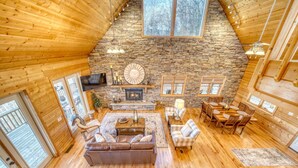 A spacious living area with a stone fireplace, wooden walls, and a high ceiling. -  Cozy Cabin with Hot Tub in Blue Ridge Mountains (Morganton)