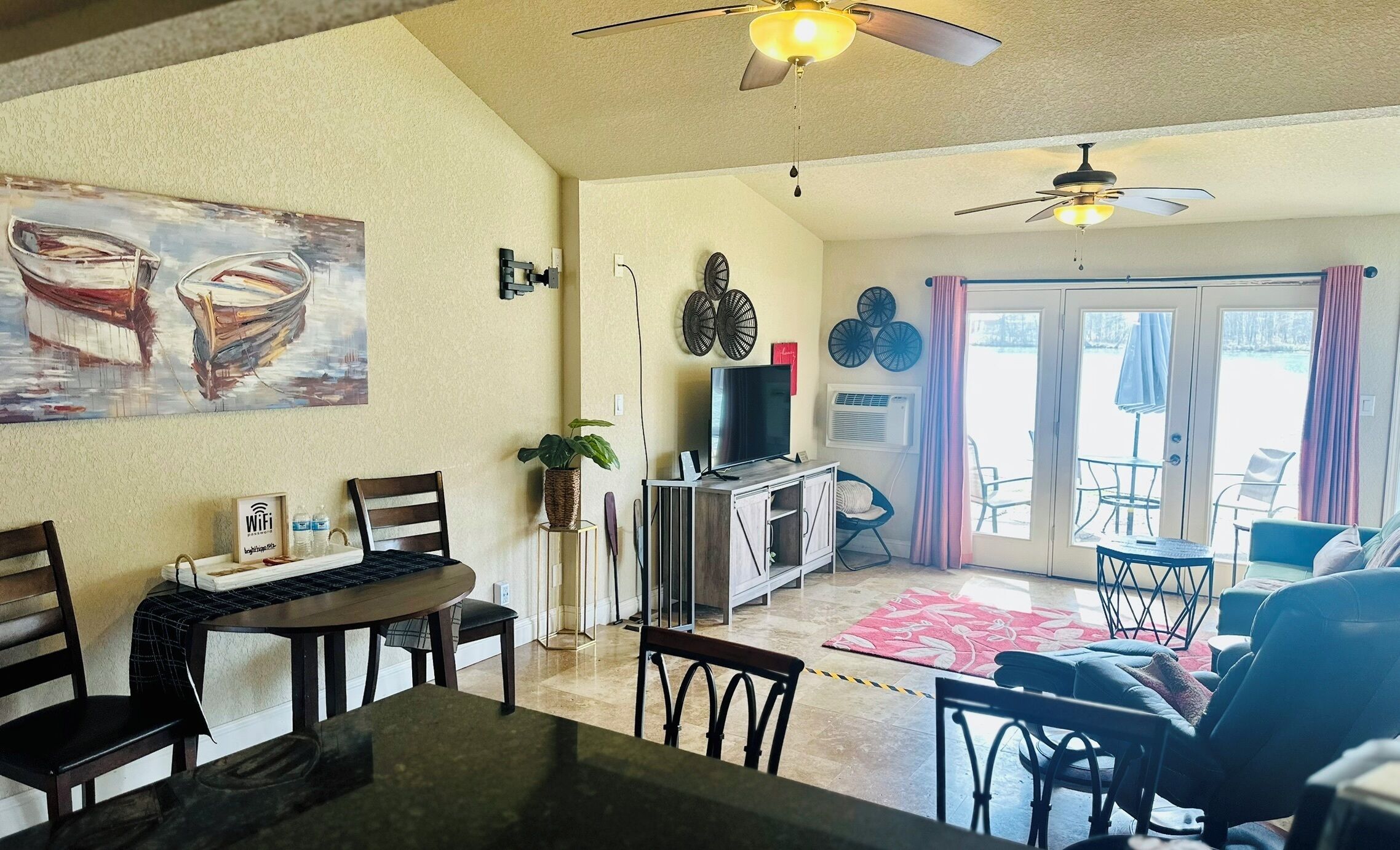 A living room with a dining area, a TV, ceiling fans, and a sliding glass door leading to an outdoor patio.