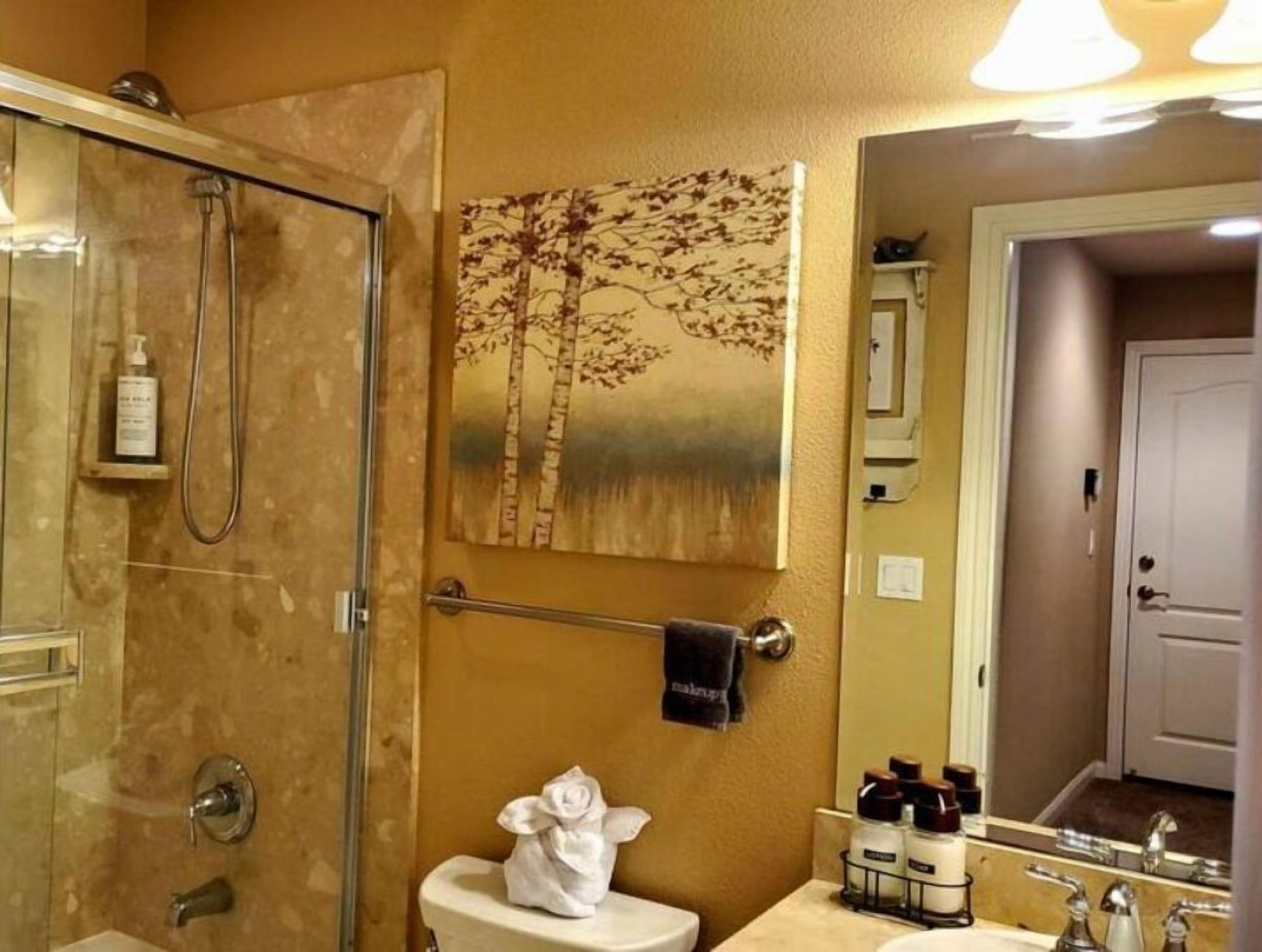 Ein Badezimmer mit Duschkabine aus Glas, Toilette mit Handtuch und Waschbecken mit Pflegeprodukten.