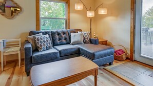 A living room with a sectional sofa, a wooden coffee table, a floor lamp, and a large window.