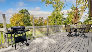 A wooden deck with a grill, outdoor table and chairs, and a covered umbrella.